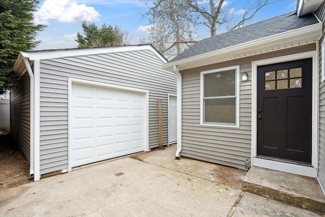 property entrance with a shingled roof, driveway, and a detached garage