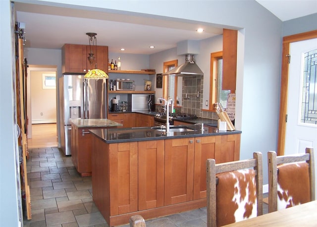 kitchen featuring stainless steel fridge, wall chimney exhaust hood, a peninsula, pendant lighting, and a sink