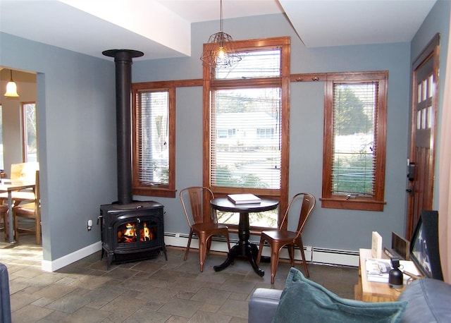 dining area featuring stone tile flooring, a wood stove, and baseboards