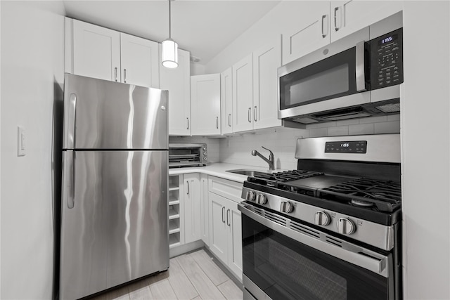 kitchen with appliances with stainless steel finishes, a sink, white cabinetry, and tasteful backsplash