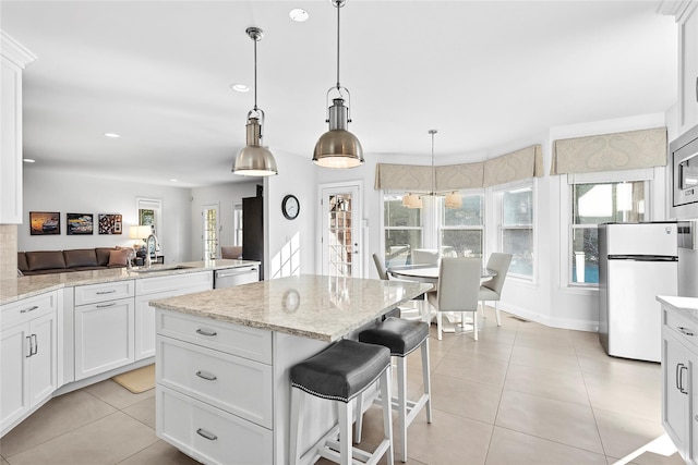 kitchen featuring a center island, light tile patterned floors, stainless steel dishwasher, freestanding refrigerator, and a sink