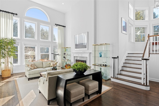 living room with stairway, a warm lit fireplace, a towering ceiling, and wood finished floors