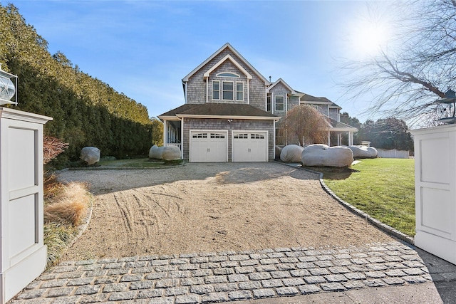 shingle-style home featuring gravel driveway, a garage, and a front yard