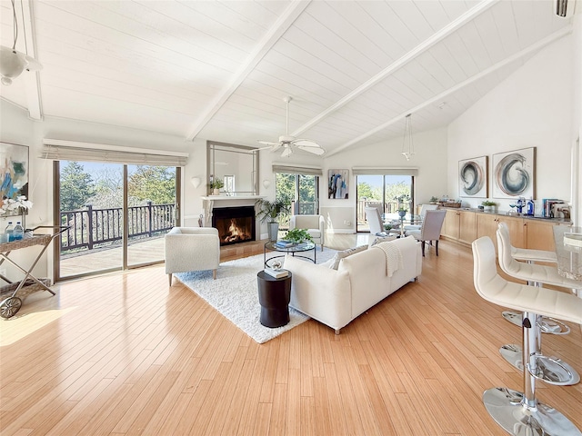 living area featuring a ceiling fan, a lit fireplace, beamed ceiling, and a healthy amount of sunlight