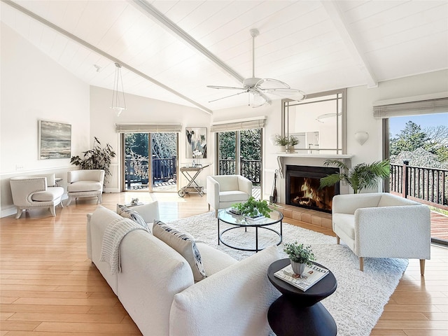 living room featuring a ceiling fan, lofted ceiling with beams, light wood-style floors, a tile fireplace, and wooden ceiling