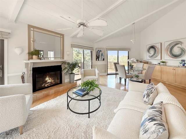 living area featuring lofted ceiling with beams, a tiled fireplace, a ceiling fan, and wood finished floors