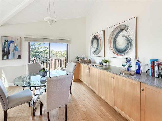 dining space featuring light wood finished floors and vaulted ceiling with beams