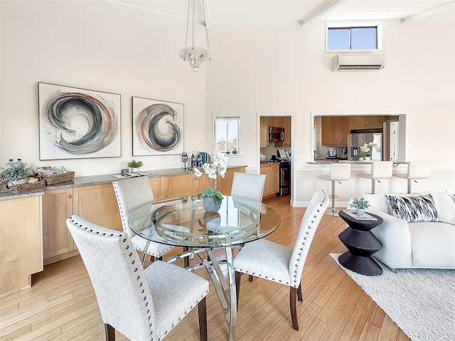 dining room with a wall mounted AC, a high ceiling, beam ceiling, and light wood-style floors