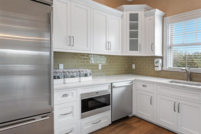 kitchen featuring dark wood-style floors, glass insert cabinets, white cabinets, a sink, and built in appliances