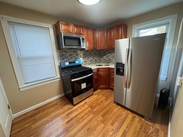 kitchen with light wood-style flooring, stainless steel appliances, a sink, light countertops, and backsplash