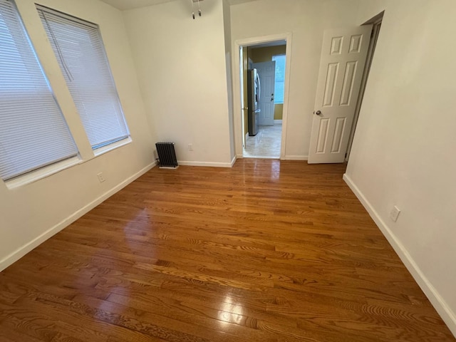 unfurnished room featuring radiator heating unit, wood finished floors, and baseboards