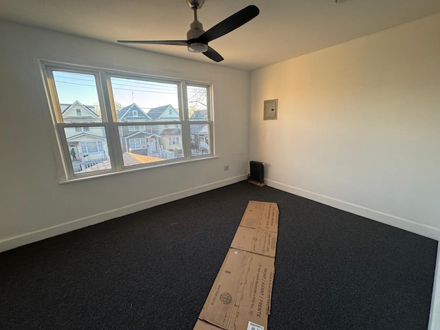 spare room with ceiling fan, baseboards, electric panel, radiator, and dark carpet