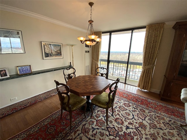 dining area featuring baseboards, hardwood / wood-style flooring, ornamental molding, a wall of windows, and a notable chandelier