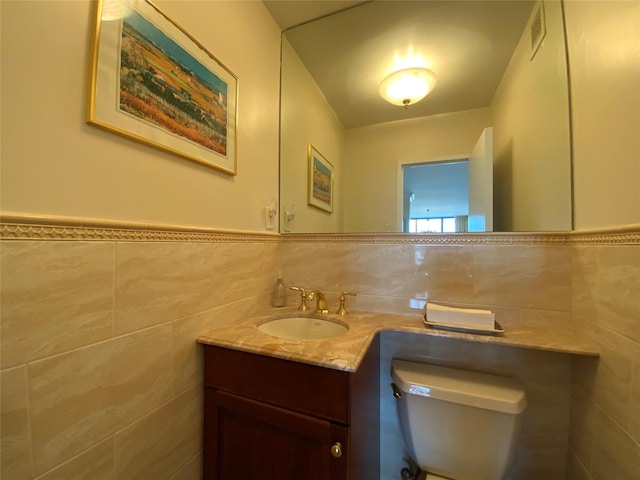 half bath featuring toilet, a wainscoted wall, visible vents, vanity, and tile walls