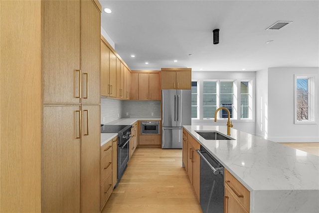 kitchen featuring visible vents, a large island, light wood-style flooring, stainless steel appliances, and a sink