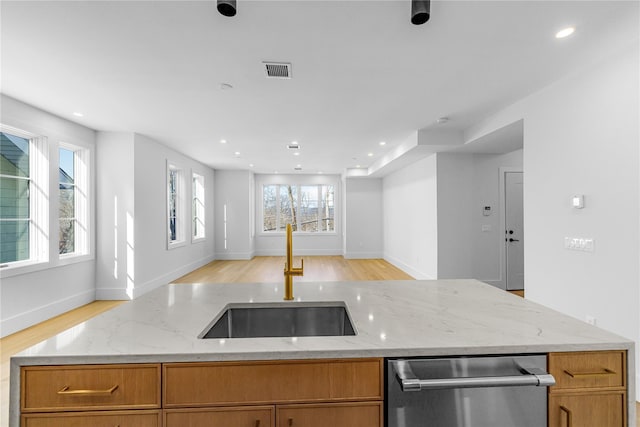 kitchen featuring brown cabinets, visible vents, stainless steel dishwasher, open floor plan, and a sink