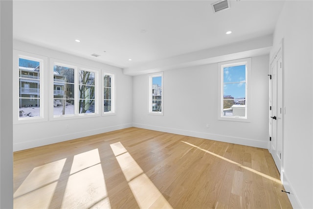 empty room featuring a wealth of natural light, light wood-type flooring, visible vents, and baseboards