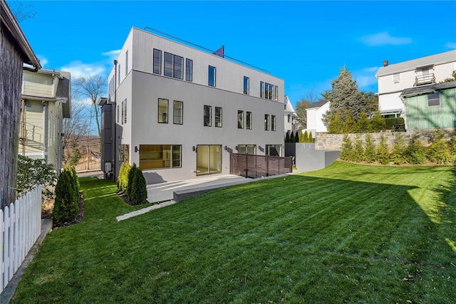 back of property with a lawn, fence, and stucco siding