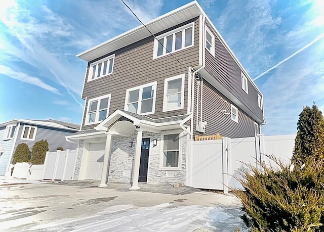 view of front facade featuring concrete driveway, stone siding, fence, and a gate