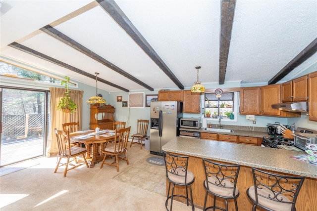 kitchen with appliances with stainless steel finishes, brown cabinets, a peninsula, under cabinet range hood, and a sink