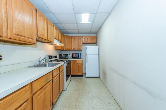 kitchen featuring white appliances, light countertops, a paneled ceiling, under cabinet range hood, and a sink