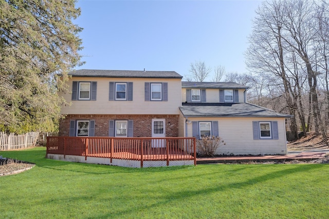 rear view of property featuring brick siding, a lawn, a wooden deck, and fence