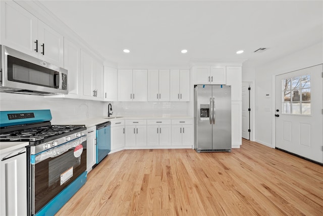 kitchen with stainless steel appliances, light countertops, light wood-style flooring, white cabinets, and a sink