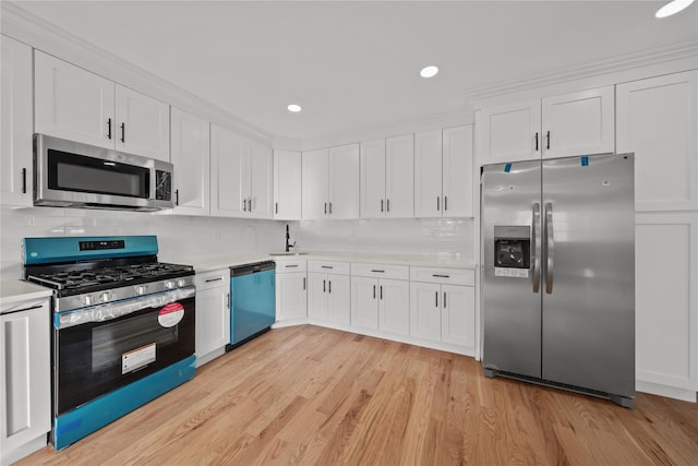 kitchen with stainless steel appliances, light countertops, white cabinetry, and light wood-style floors