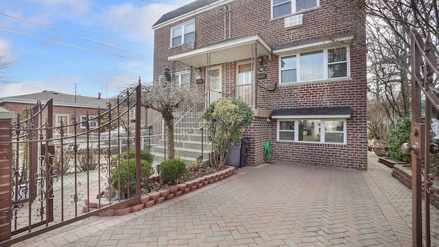 view of front of home featuring brick siding, fence, and stairs