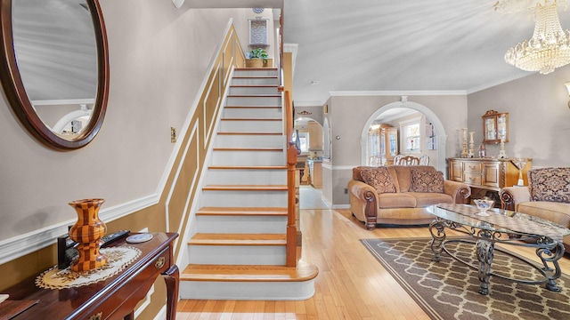 staircase featuring ornamental molding, arched walkways, a notable chandelier, and hardwood / wood-style floors