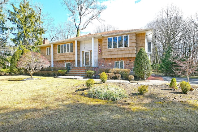 bi-level home with brick siding, a chimney, and a front yard