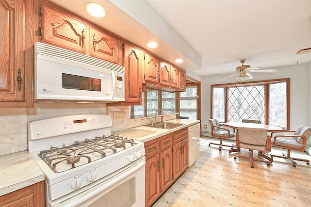 kitchen featuring light floors, light countertops, brown cabinetry, white appliances, and a sink