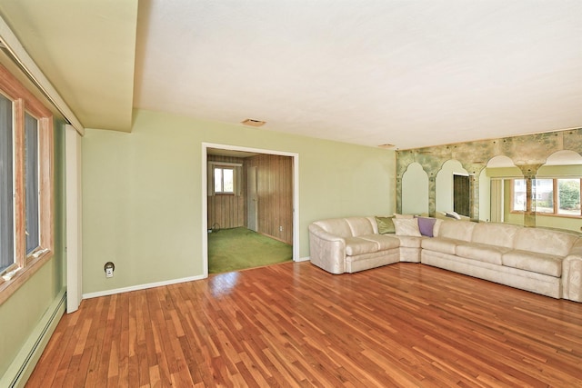 unfurnished living room featuring a baseboard heating unit, wood finished floors, visible vents, and baseboards