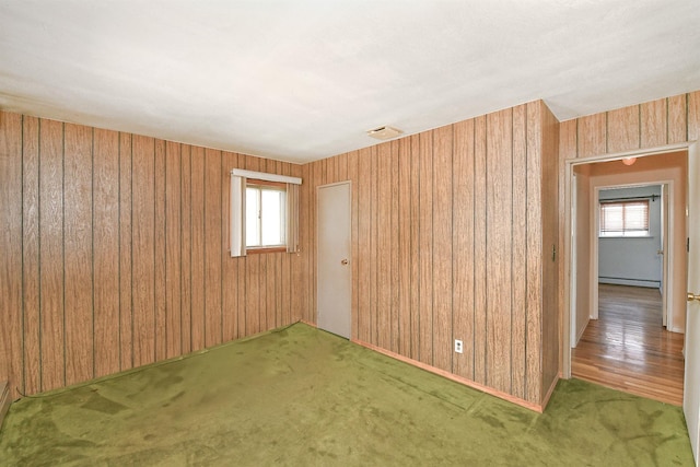 spare room with a baseboard heating unit, wooden walls, carpet, and visible vents