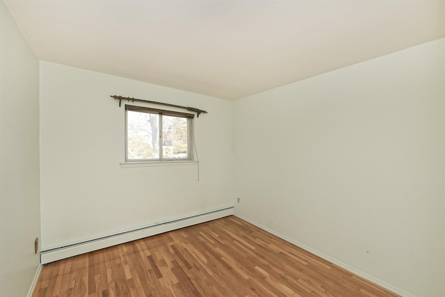 empty room featuring a baseboard heating unit, baseboards, and wood finished floors