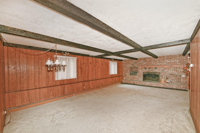 unfurnished living room featuring beam ceiling, wood walls, carpet flooring, a fireplace, and a healthy amount of sunlight