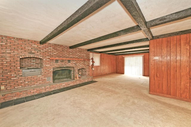 unfurnished living room with beam ceiling, wood walls, a brick fireplace, and carpet floors