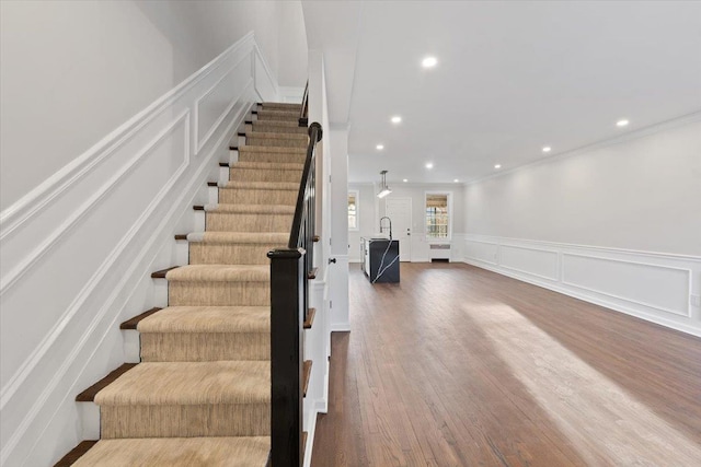 stairway featuring recessed lighting, wood finished floors, and a decorative wall