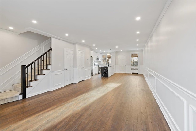 unfurnished living room with crown molding, stairway, recessed lighting, wood finished floors, and a decorative wall