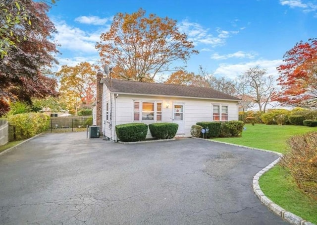 view of front of property featuring aphalt driveway, a chimney, central AC unit, fence, and a front lawn