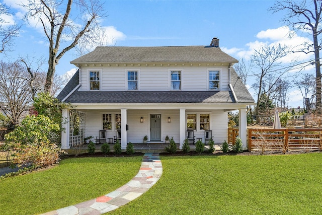 view of front of home with a front yard, covered porch, roof with shingles, and a chimney