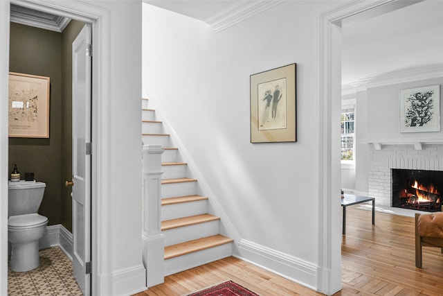 stairs featuring hardwood / wood-style flooring, a brick fireplace, baseboards, and ornamental molding