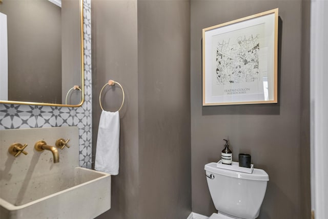 half bathroom with a sink, backsplash, and toilet