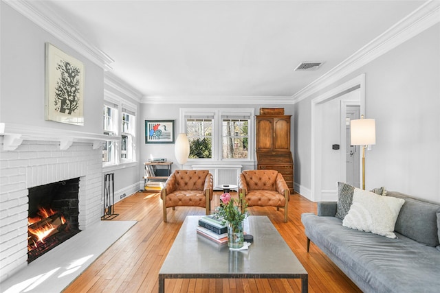 living area with visible vents, a fireplace, light wood-type flooring, and crown molding