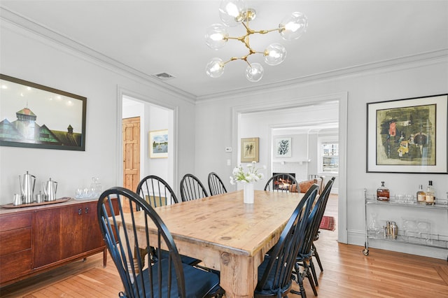 dining room with visible vents, light wood-style flooring, a fireplace, ornamental molding, and a notable chandelier