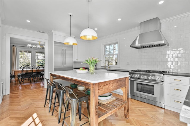 kitchen with light stone countertops, high quality appliances, wall chimney range hood, and ornamental molding