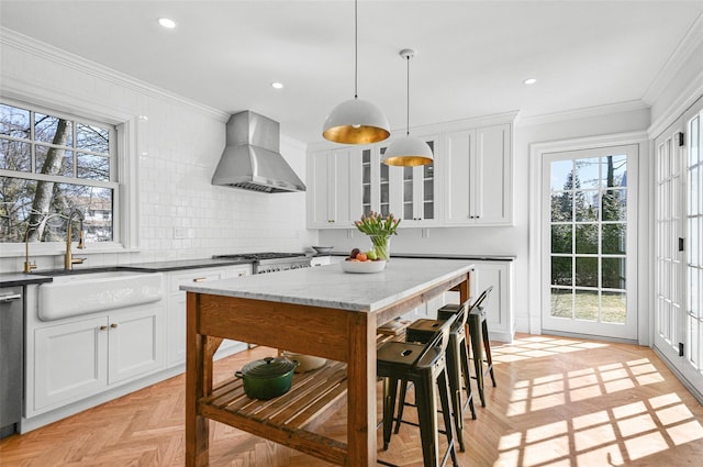 kitchen with backsplash, glass insert cabinets, wall chimney range hood, ornamental molding, and a sink