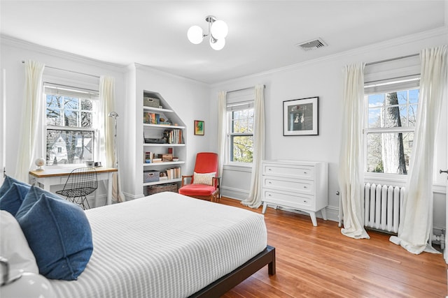 bedroom featuring visible vents, radiator, baseboards, ornamental molding, and wood finished floors