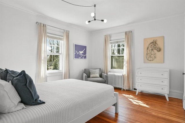 bedroom featuring an inviting chandelier, radiator heating unit, wood finished floors, and ornamental molding