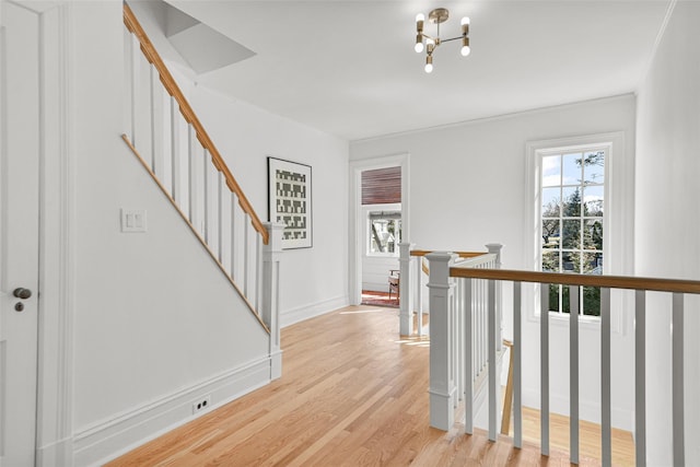 corridor featuring an upstairs landing, a chandelier, baseboards, and light wood-style flooring